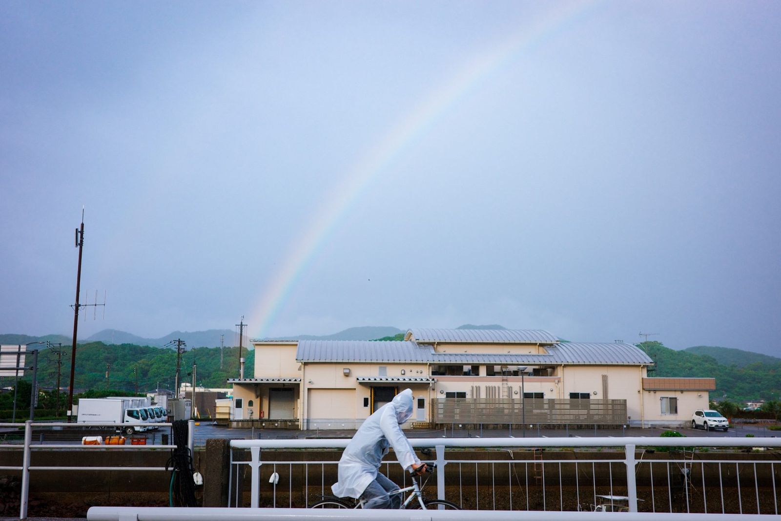 雨上がりの虹と、レインコートで自転車をこぐ人