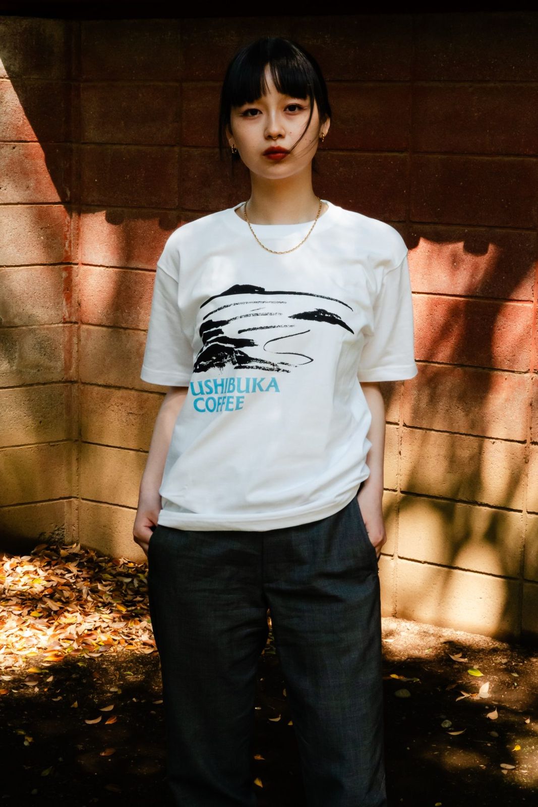 水墨画の風景とUSHIBUKA COFFEEのロゴが入ったTシャツを着た女性